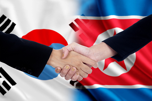 Two workers shaking hands after negotiation in front of the north and south korean flags