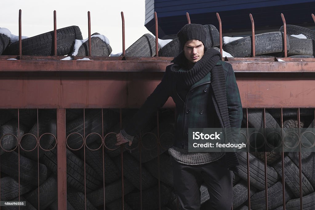young fashion man poses outdoor picture of a young fashion man posing by a tire centre while looking into the camera Adult Stock Photo