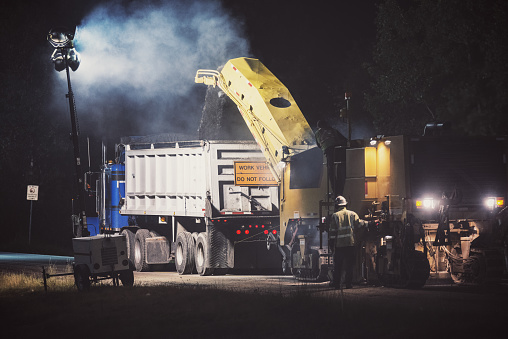 A construction crew works into the night on a road repaving project.  Long exposure.