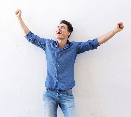 Portrait of a cheerful young man with raised arms celebrating