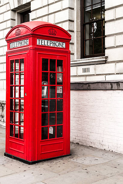 London, UK - June 22, 2018: People tourists standing looking at red telephone box booth on Piccadilly sidewalk street road in downtown city holding phone family