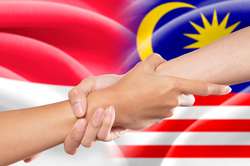 Hand grabbing a person hand for helping in front of the indonesian and malaysian flags