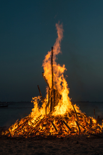 Easter fire at the beach of the harbor of Hamburg - Germany. Flames and dark smoke are rising in the clear sky. The river Elbe in the background.