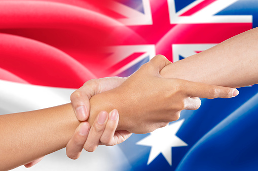 Helping hands, a hand pulling a person hand in front of the indonesian and australian flags