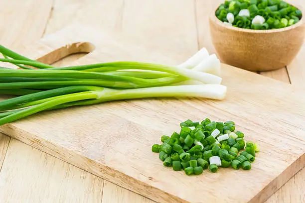 Chopped spring onions on wooden cutting board.