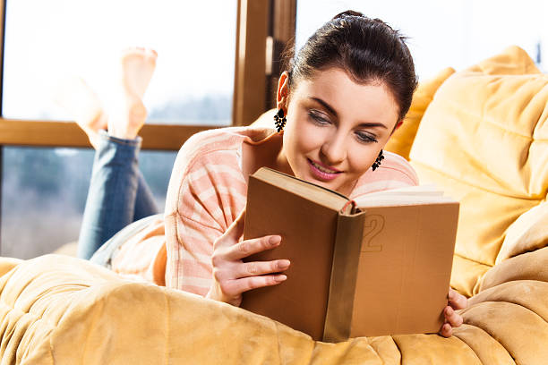 istock Woman lying on her couch reading a book at home 486716498