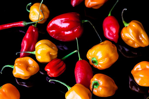 Scattered yellow and red habanero peppers on black background from above