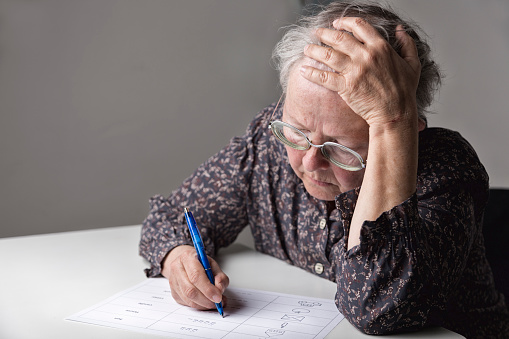 Illiterate woman is learning how to write, sitting at table. Learning material in English language, created by Silvia Jansen