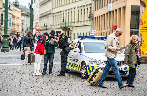 Prague, Czech Republic - May 3, 2015: Policeman showing direction to Asian tourists in Prague, couple of tourists with suitcase walking nearby