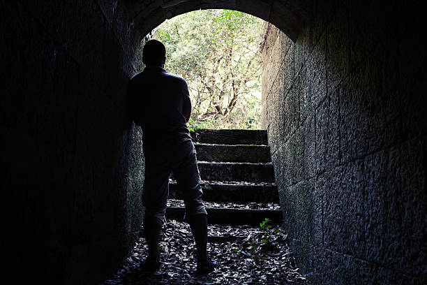 istock Man stands in dark stone tunnel with glowing end 486722502