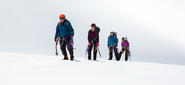 Four People Staying on Mountain High Altitude Snowfield Sporty Clothing and Safety Climbing Gear Mature Male Guide and Young Female Athletes