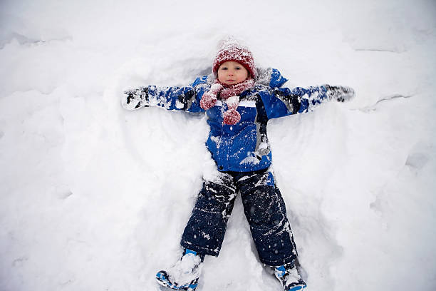Adorable little boy in blue jacket, red hat and scarf,  lying on north pole snow, making snow angel