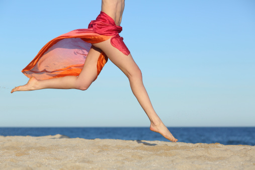 Woman legs jumping on the beach happy with the horizon and sea in the background