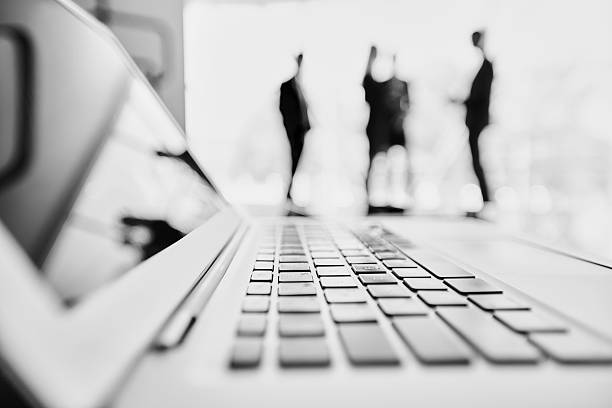Cooperation behind laptop Open laptop on foreground and defocused silhouettes of business people in the background incidental people photos stock pictures, royalty-free photos & images
