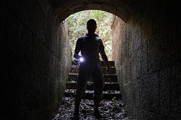 istock Young man with a flashlight enters stone tunnel 486737918
