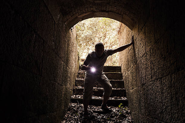 istock Young man with a flashlight enters the stone tunnel 486738334