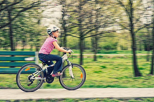 Panning shot of little girl riding a bike through a park.