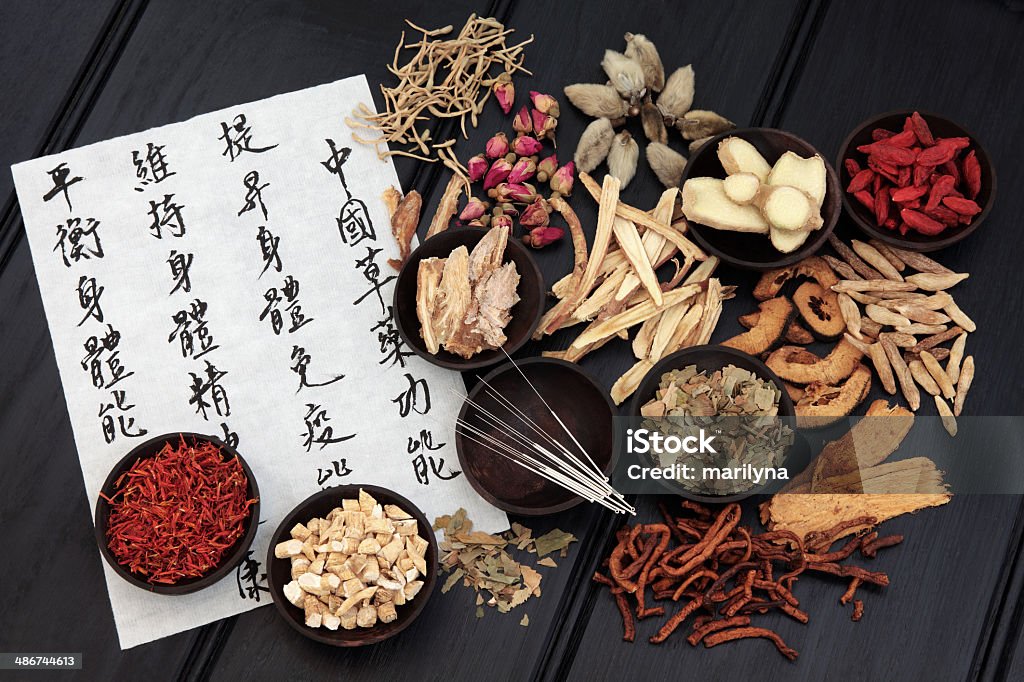 Traditional Chinese Medicine Acupuncture needles with chinese herbal medicine selection and mandarin calligraphy script on rice paper describing the medicinal functions to maintain body and spirit health and balance body energy. Chinese Herbal Medicine Stock Photo