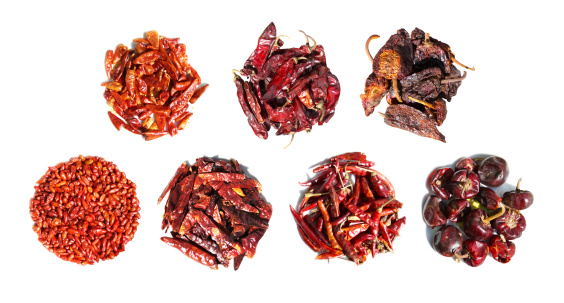 Various types of dried red chiles in piles on white background