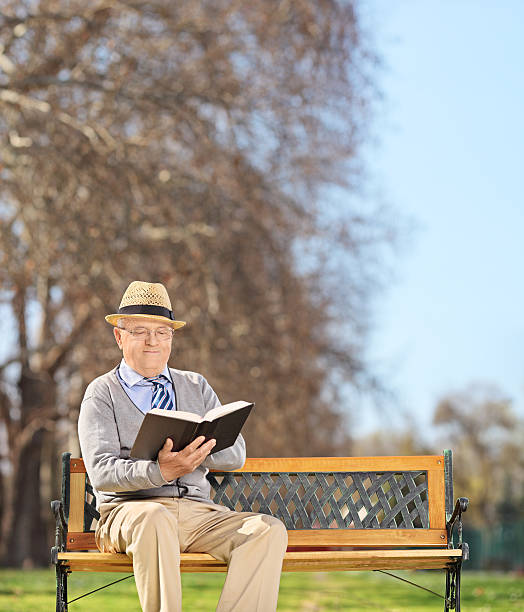 istock Senior sitting on bench and reading book in park 486749659