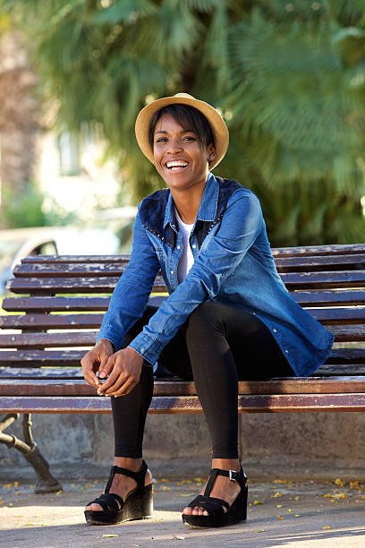 Portrait of a smiling young black woman sitting on bench at the park