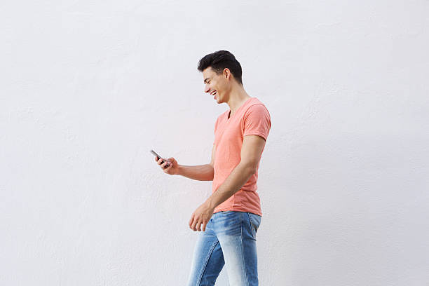 istock Smiling young man walking and looking at cell phone 486784744