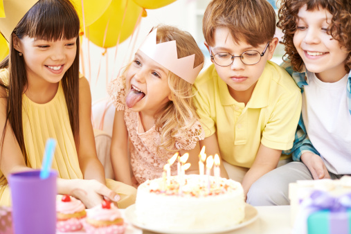 Four cheerful children gathered around birthday cake with burning candles