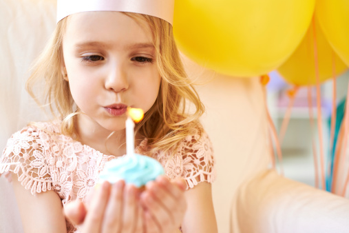 Cute little girl blowing out candle on cupcake
