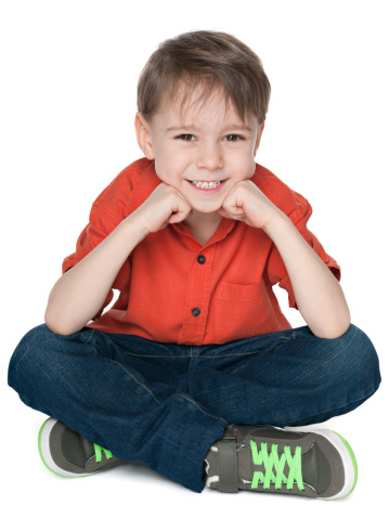 A happy little boy in the red shirt is sitting on the white background