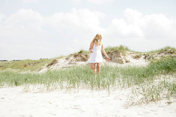 Girl walking through beach dunes at sunset