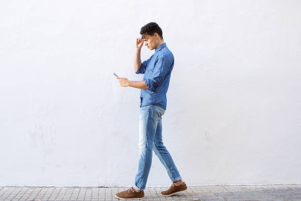 istock Young man walking and reading text message on cell phone 486790216