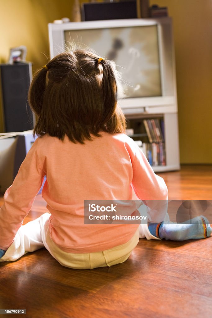 Watching TV Rear view of little girl sitting on the floor and watching cartoons on TV at home   Note to inspector: the image is pre-Sept 1 2009 2015 Stock Photo