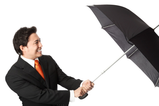 Businessman in a suit and tie, holding an umbrella trying not to blow away. White background.