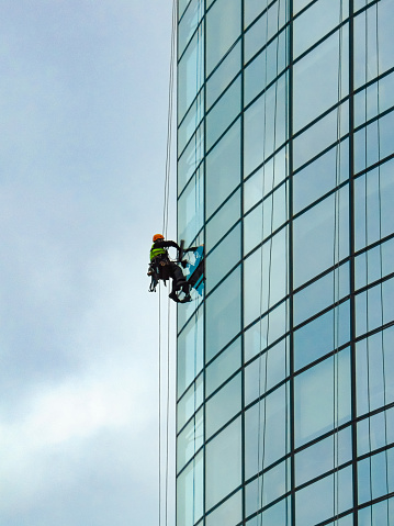 Window cleaner working at heights on glass skyscraper edge.