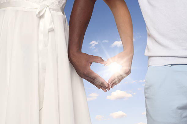 Young Couple Crossing Their Arms and Forming a Heart Shaped Hands Together Against sunny blue sky
