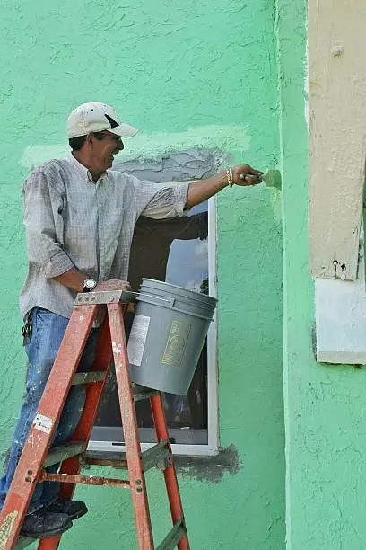 A handyman smiles as he paints on a ladder
