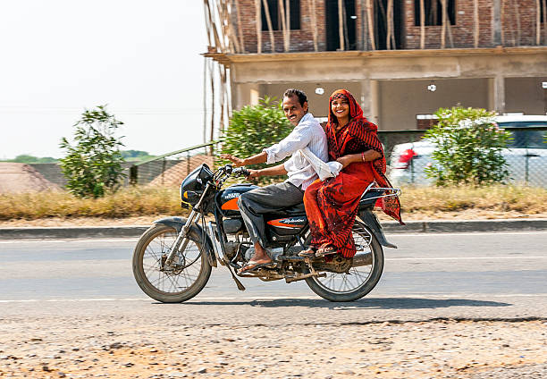 Agra, India - October 17, 2012: friendly greeting couple riding on scooter riding on scooter through busy highway in Rajasthan, India. Up to six family members manage to ride these two wheelers.
