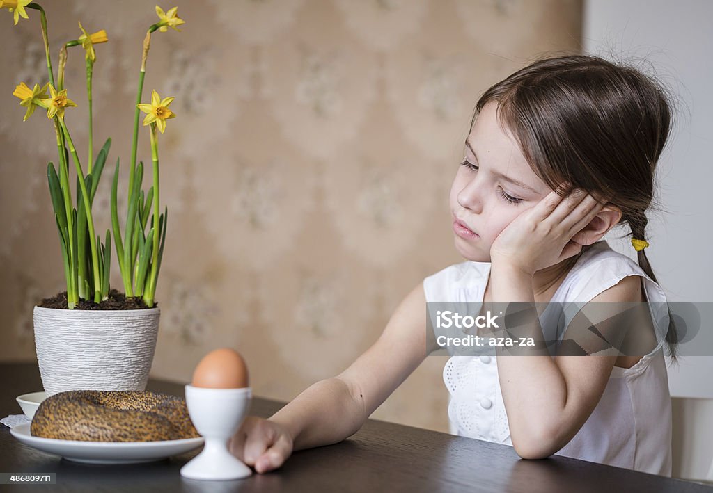 Thoughtful preschooler girl refusing to eat Thoughtful preschooler girl sitting at the table in the kitchen with pot flowers No Appetite Stock Photo