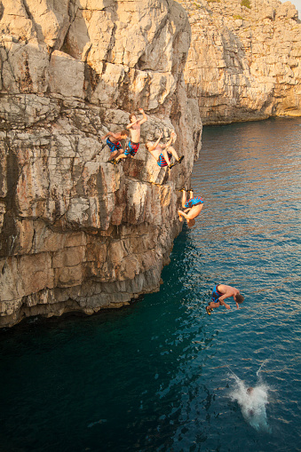 Young man cliff diving into deep sea. He is jumping back somersault. Sequence image merged from 6 exposures.