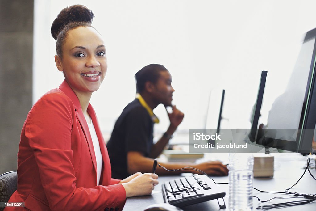 Young students at college computer lab Happy young african american woman sitting in front of computer smiling at camera. Young students sitting at table using computers at school. Computer Lab Stock Photo