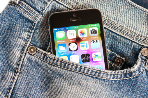 Udine, Italy - April 21, 2014: iPhone 5s model showing the home screen with iOS7 popping out from the pocket go a pair of blue vintage denim trousers