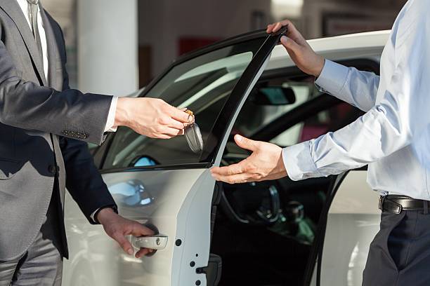 a person handling a car key to another person, trading a car at a dealership
