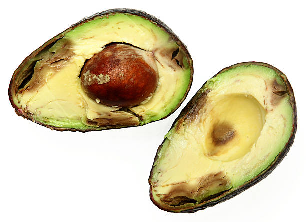Overly Ripe Avocado Sliced with Seed Over White Overly Ripe Spotted Avocado Sliced with Seed Over White avocado brown stock pictures, royalty-free photos & images