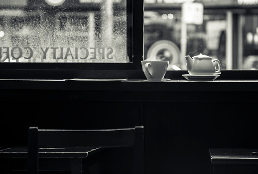 Cup of hot tea and teapot with a visible light steam at the window of the coffee shop as a metaphor of warm place safe from the troubles of outside world