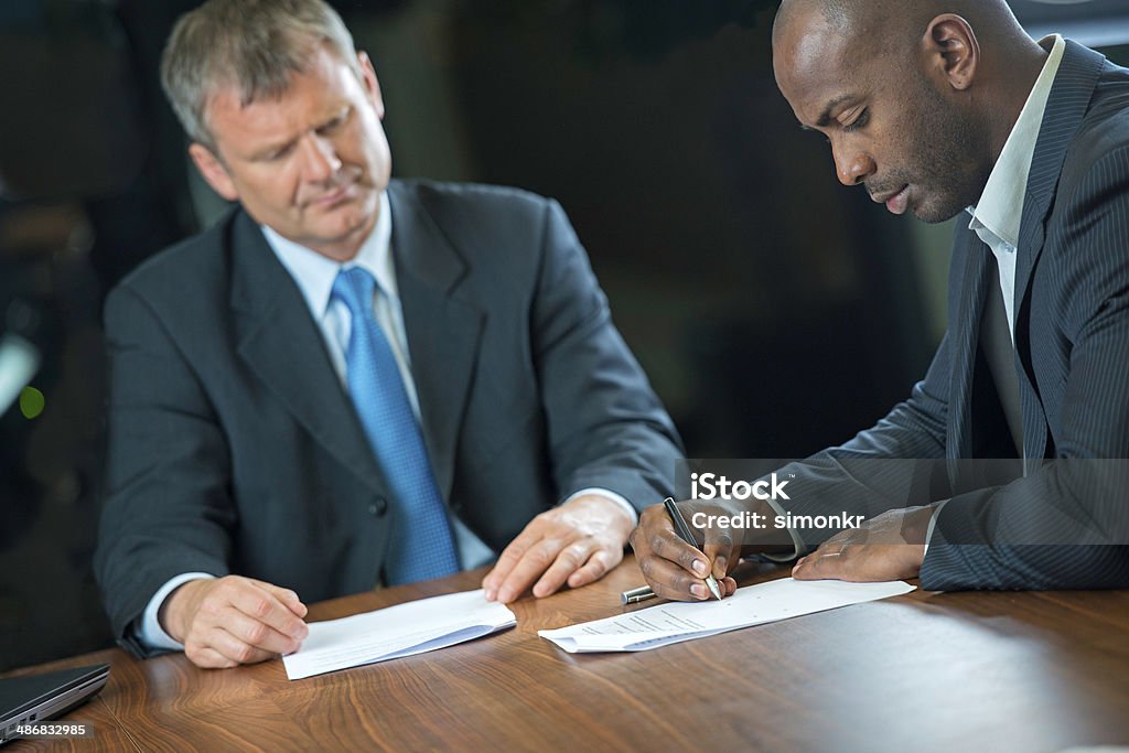 Businessmen Signing Papers Two businessmen signing papers and shaking hands. Adult Stock Photo