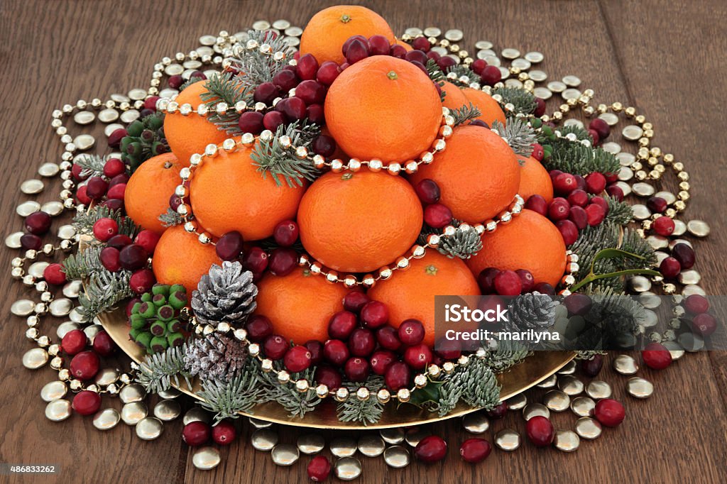 Christmas Fruit Scene Christmas satsuma orange and cranberry fruit, gold bead and smartie decorations, holly, mistletoe and winter greenery over oak background. 2015 Stock Photo