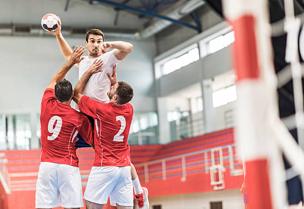 Handball player shooting at goal. Young handball player is shooting at a goal, while his opponents are holding him.    team handball stock pictures, royalty-free photos & images