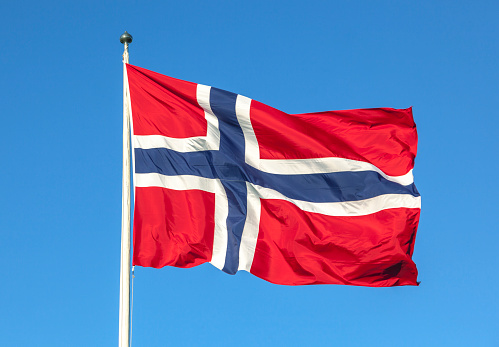 Norwegian flag in red white and blue agianst the sky.