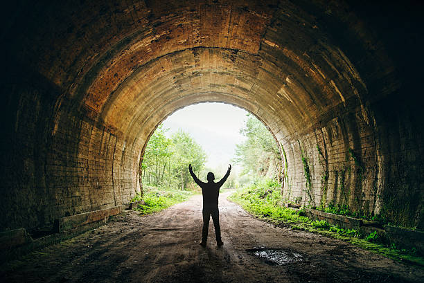 Light at the end of the tunnel A young man stands ith arms wide open against the exit of a dark tunnel. the end stock pictures, royalty-free photos & images