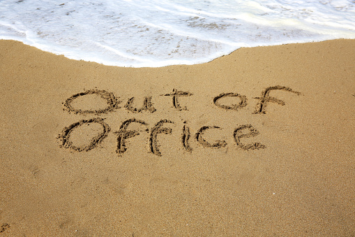 Out of office, a message written in the sand at the beach. 